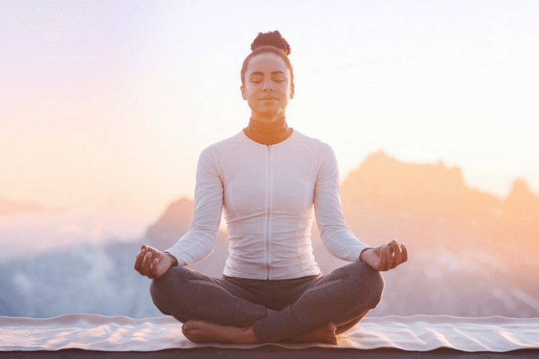 Person meditating on a mountain at sunrise, symbolizing stress reduction and inner calm.