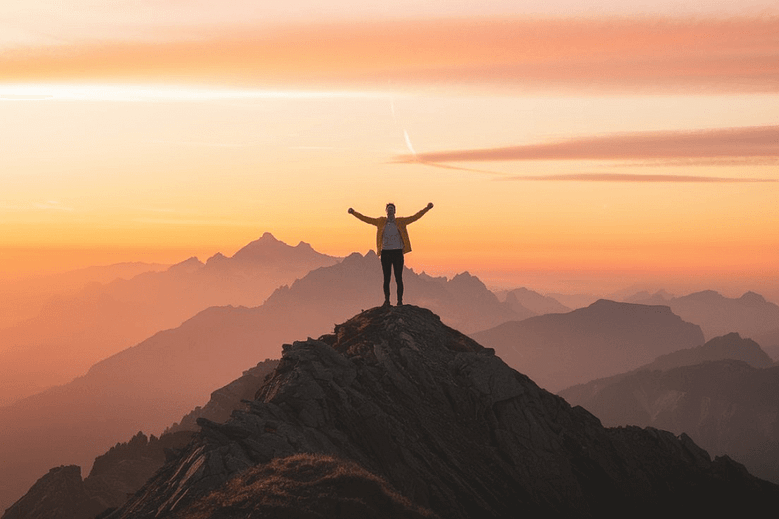 Person standing on a mountain peak at sunrise, symbolizing success and personal growth.